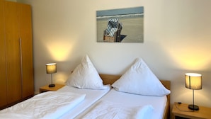 Habitació d'hotel amb un llit, dues làmpades de nit, un armari de fusta i un quadre amb una escena de platja a la paret.