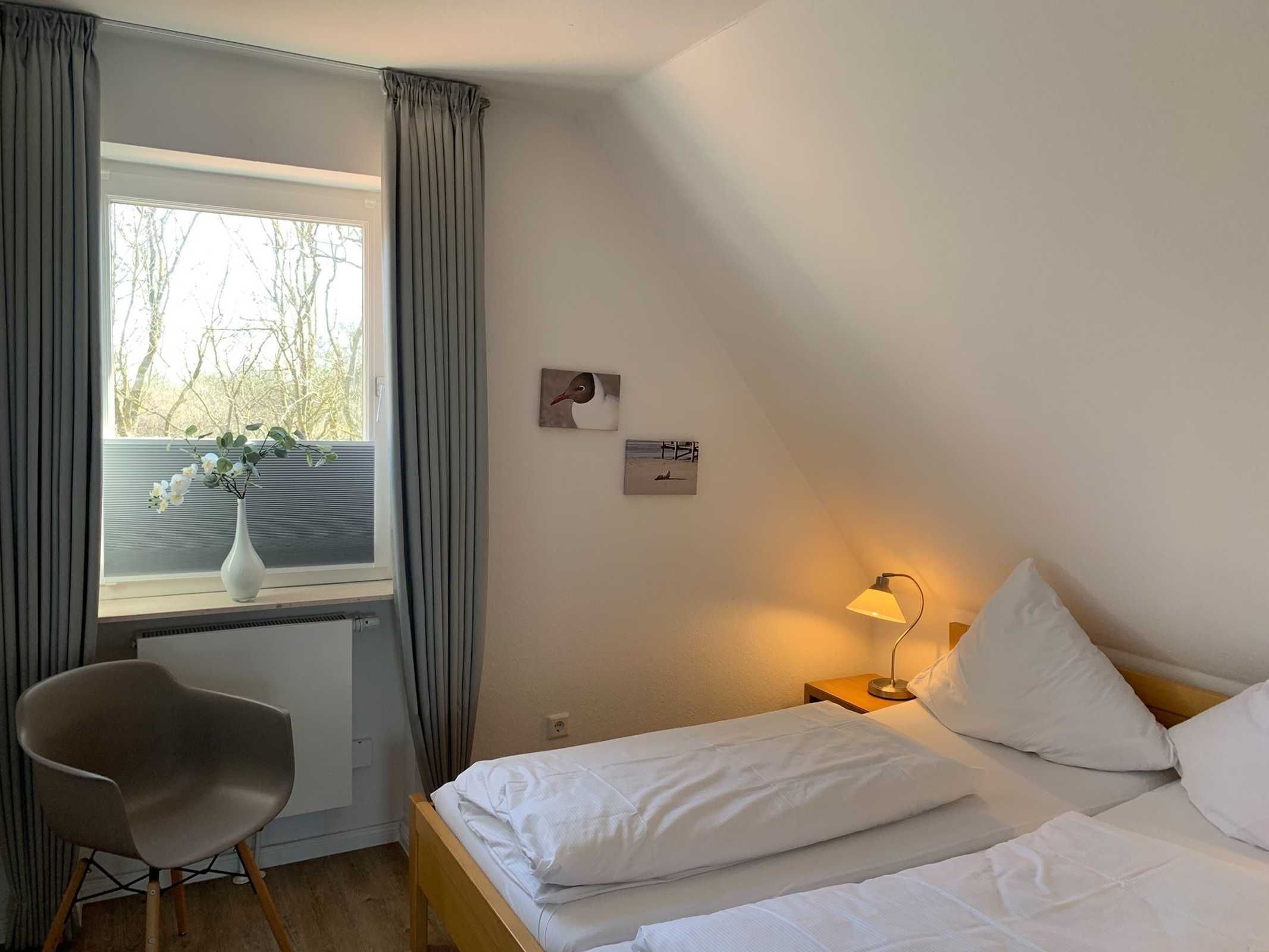 Ett hotellrum med en säng, en stol, ett fönster med gardiner och en lampa.