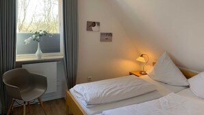 A hotel room with a bed, a chair, a window with curtains, and a lamp. - Luna IV - Luna apartment 36 (Sankt Peter-Ording)
