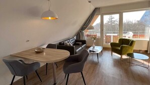A modern living room with a dining area, a sofa, two armchairs, and a small table. - Luna IV - Luna apartment 36 (Sankt Peter-Ording)