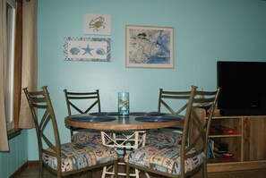 Un comedor con una mesa redonda de madera, cuatro sillas con tapicería estampada y un jarrón azul.