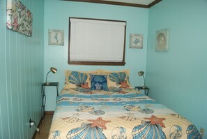 Un dormitorio con cama, dos mesitas de noche, una ventana con persianas y adornos en la pared.