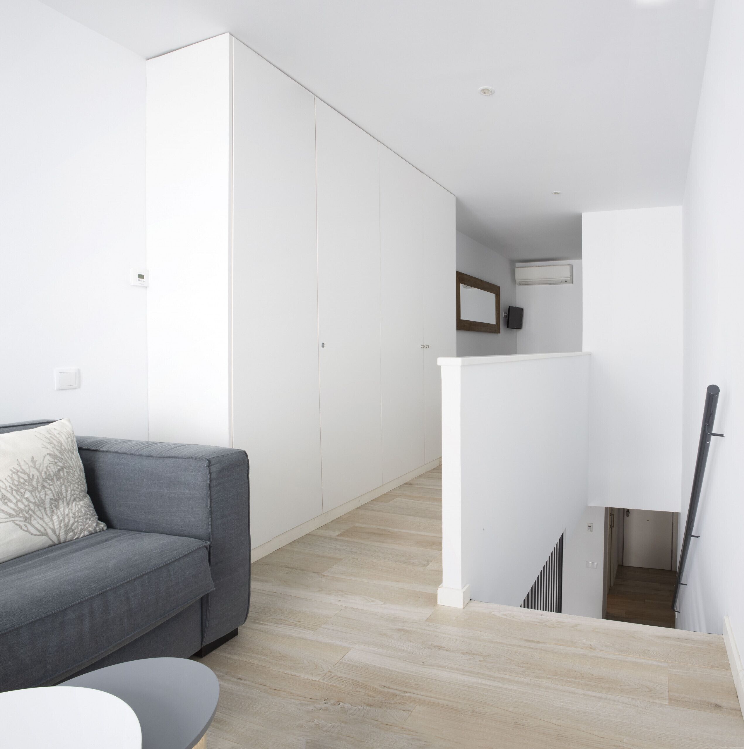 Una sala moderna con un sofá gris, una mesita redonda y un armario blanco.