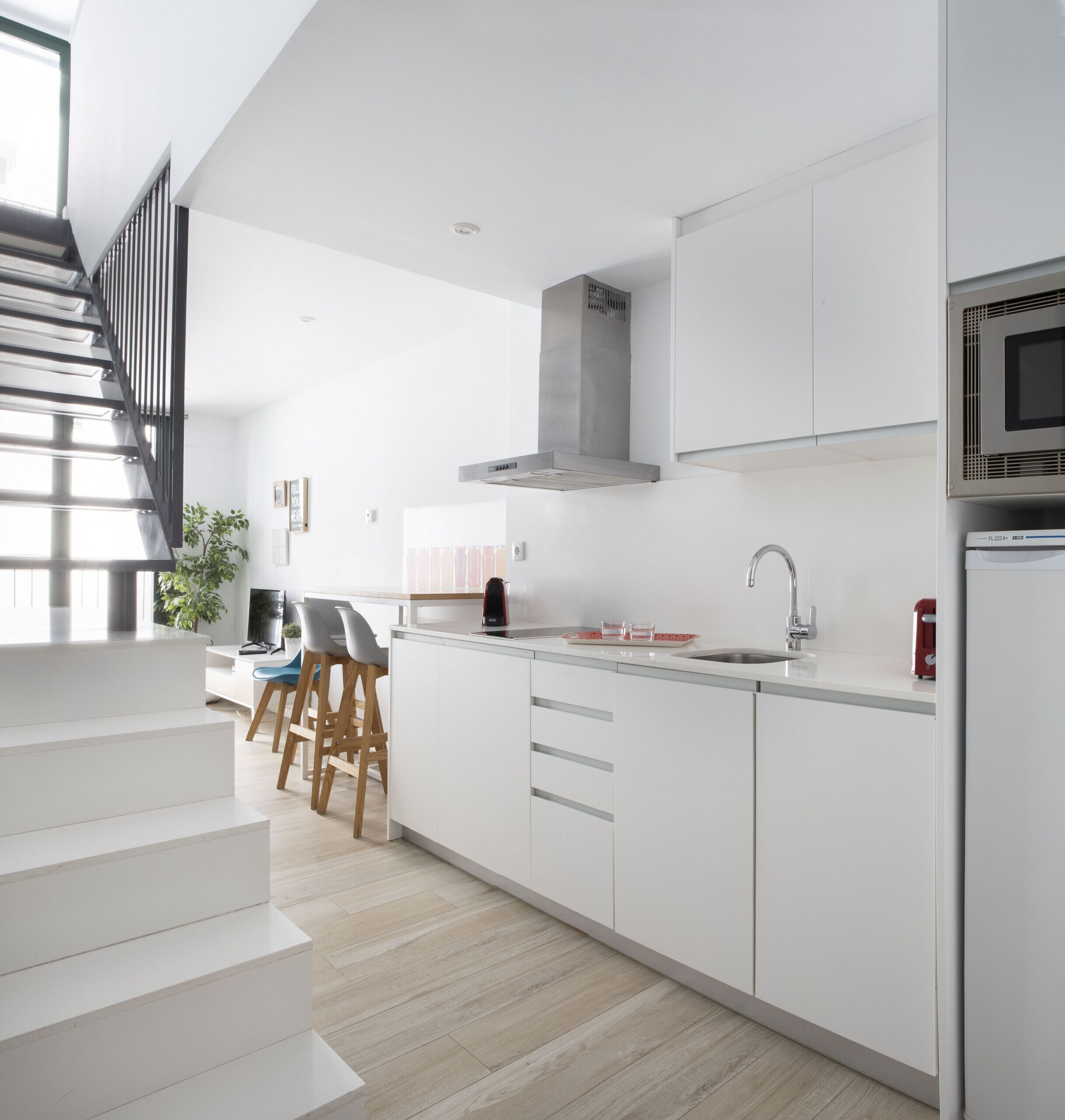 A modern kitchen with white cabinetry, a stainless steel range hood, and a built-in microwave.