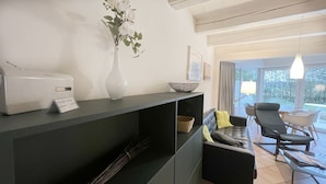 A modern living room with a dark sofa, a coffee table, a vase with flowers, a bowl, and a lamp. - Luna20 (room category) - Luna II (Sankt Peter-Ording)