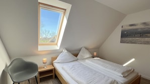 A small, well-lit room with a bed, a chair, a nightstand, and a window. - Luna20 (room category) - Luna II (Sankt Peter-Ording)