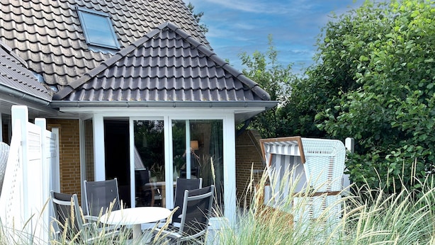 A house with a tiled roof, a covered porch with chairs, and a table. - Luna20 (room category) - Luna II (Sankt Peter-Ording)