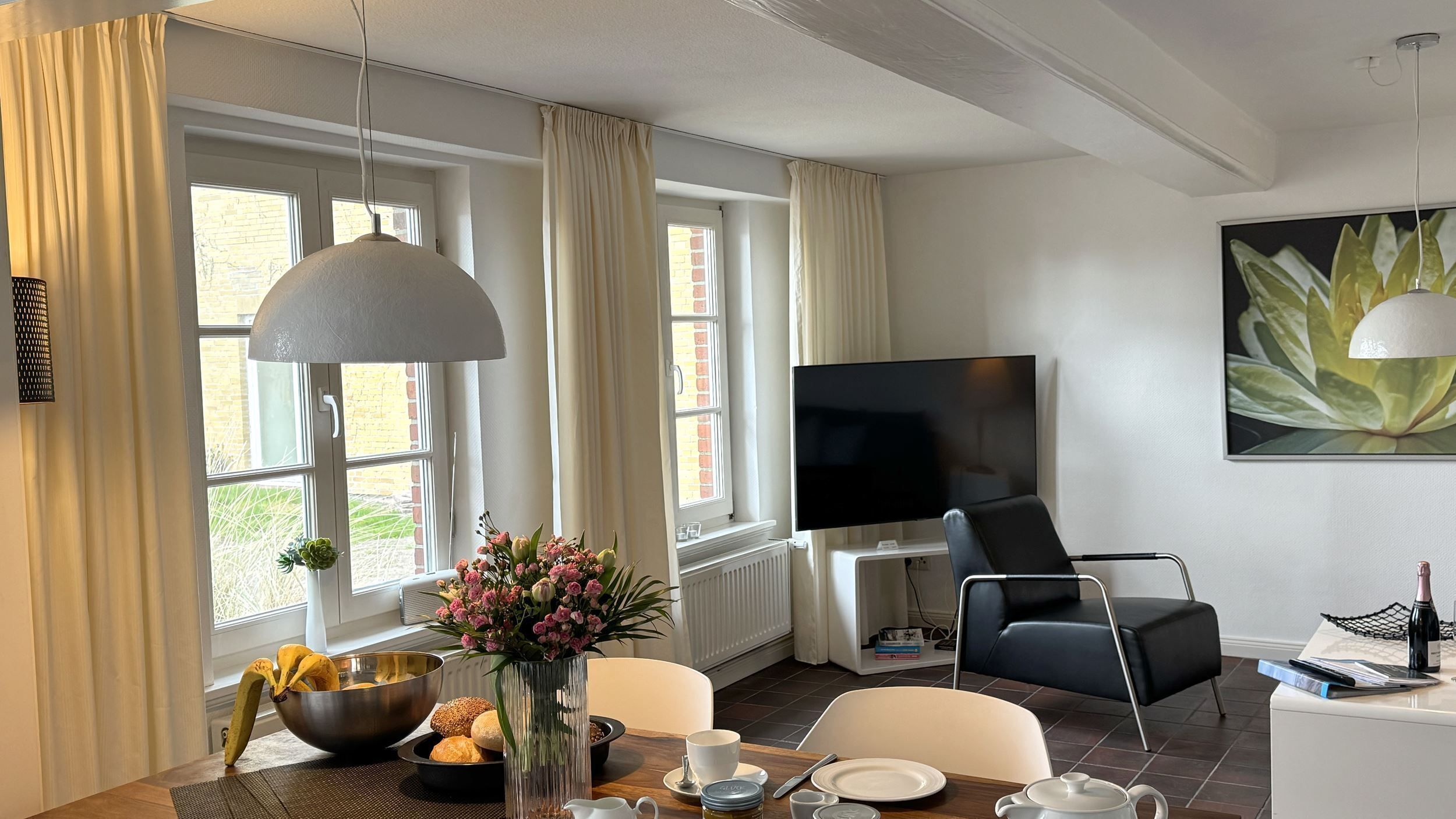 A modern hotel room with a dining area, a TV, and a large window with curtains.