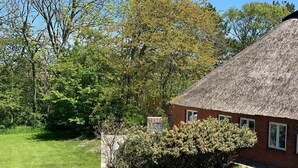 A thatched-roof house with a well-maintained lawn and dense shrubbery. - Luna12 (Room category) - Luna I (Sankt Peter-Ording)