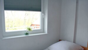 A small, single-bed room with a window and a small table with a vase of flowers. - Luna12 (Room category) - Luna I (Sankt Peter-Ording)