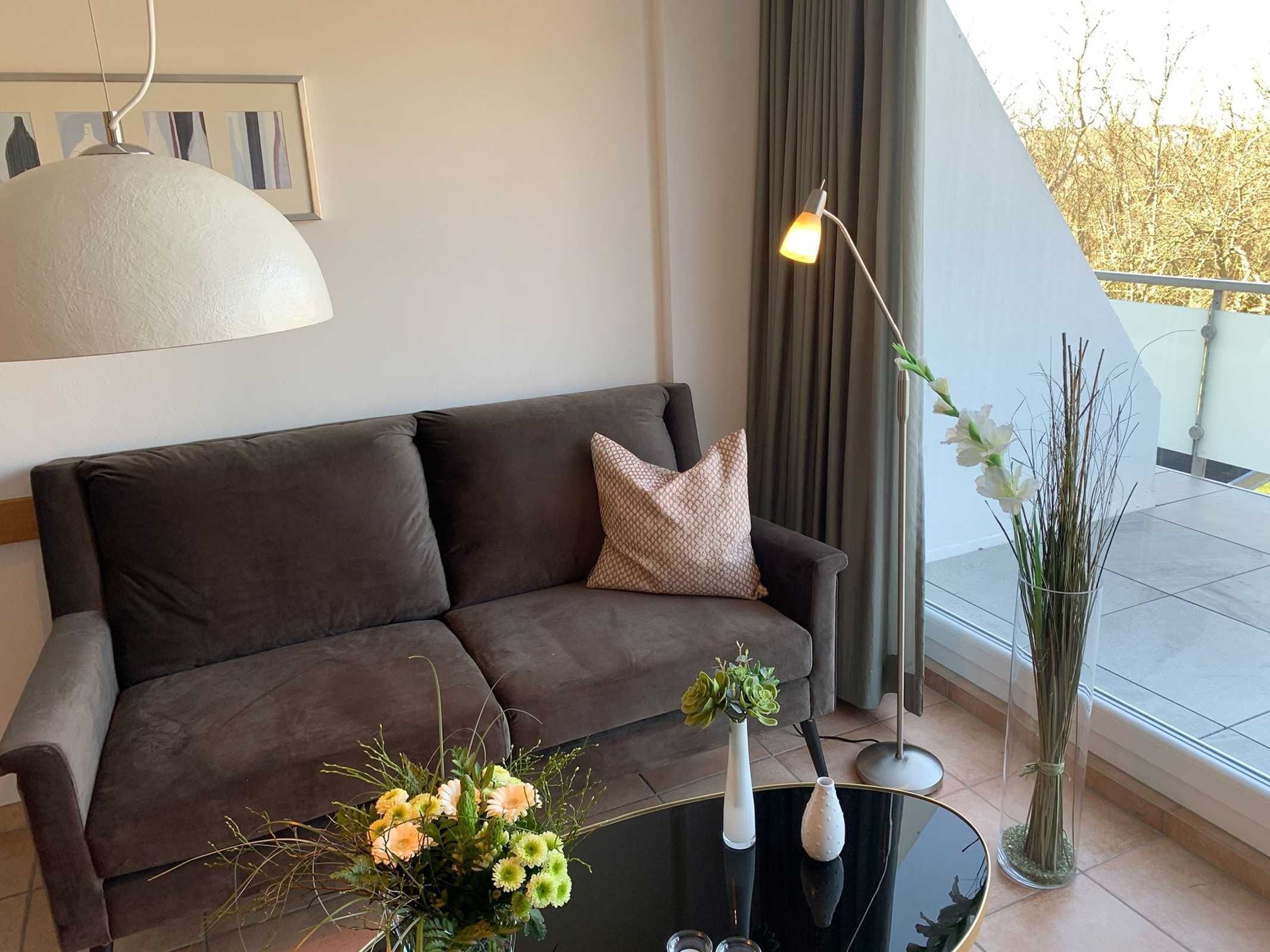 A modern living room with a dark brown sofa, a glass coffee table, and two vases with flowers.