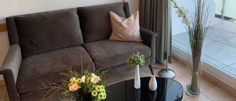 A modern living room with a dark brown sofa, a glass coffee table, and two vases with flowers.