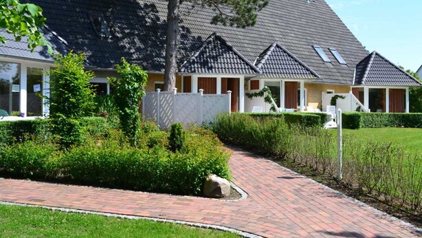 A building with a sloped roof, a brick pathway, and well-maintained greenery. - Luna12 (Room category) - Luna I (Sankt Peter-Ording)