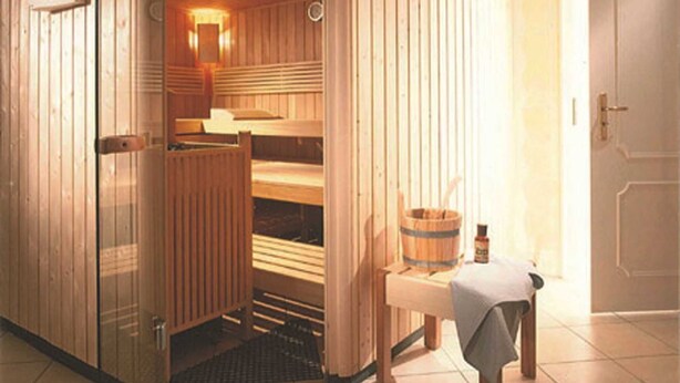 Sala de sauna com paredes de madeira, bancos e uma pequena mesa com toalha.