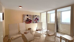 Um quarto com quatro cadeiras brancas, uma mesinha e duas pinturas abstratas na parede.