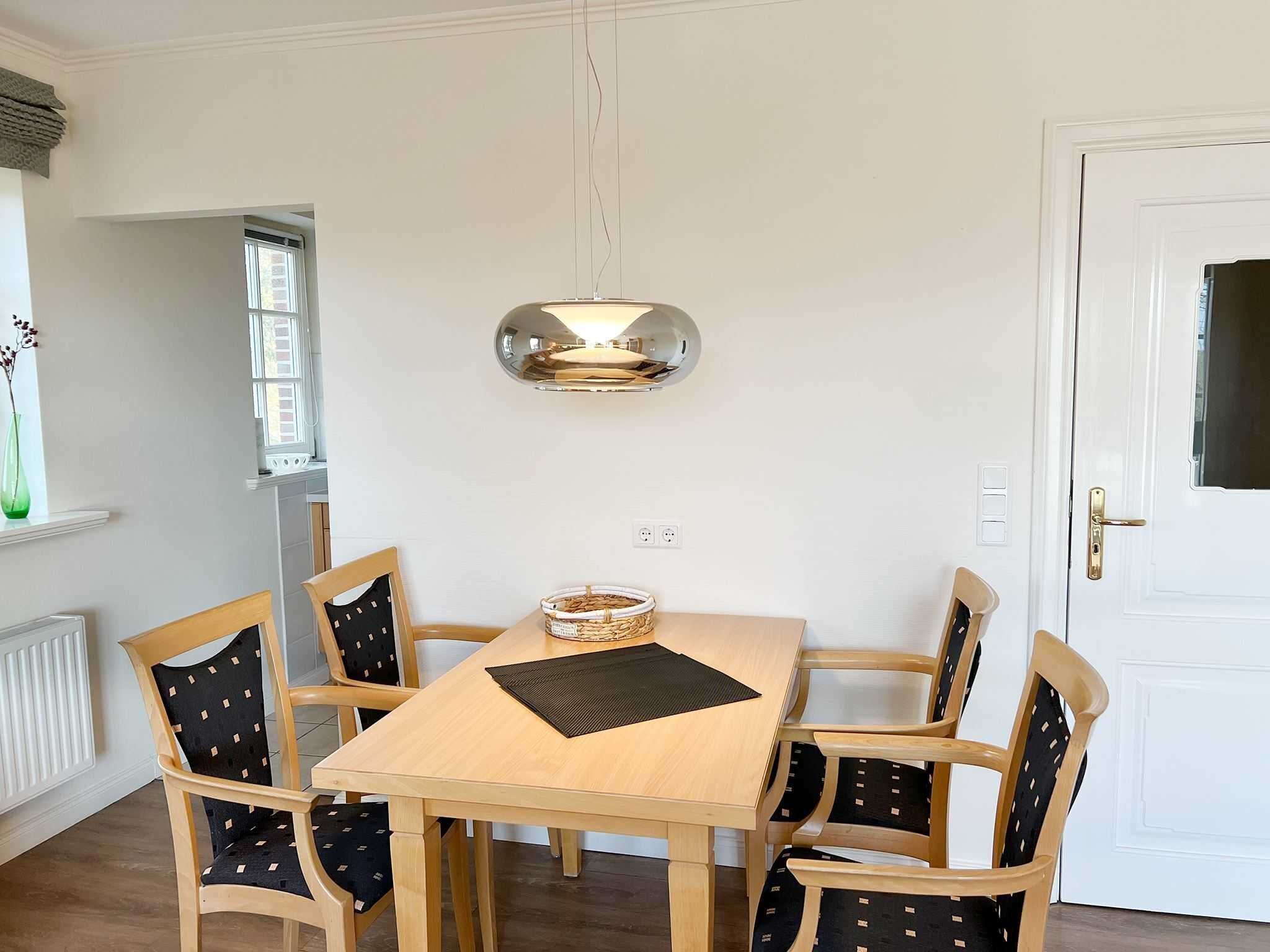 A dining area with a wooden table and six chairs, a hanging light fixture, and a window with a view.