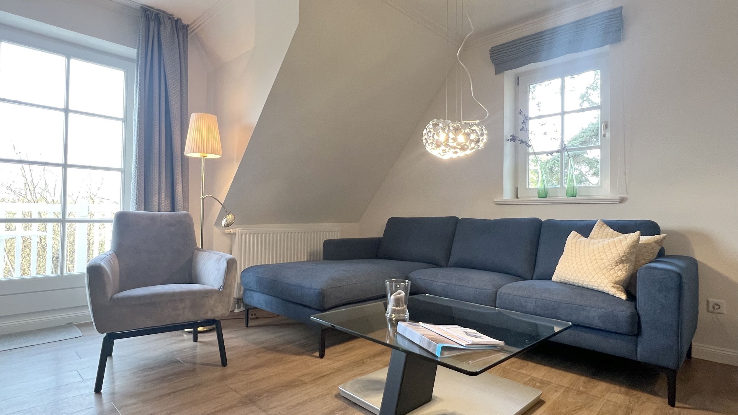 Ett modernt vardagsrum med en grå soffa, ett soffbord i glas och en golvlampa.
