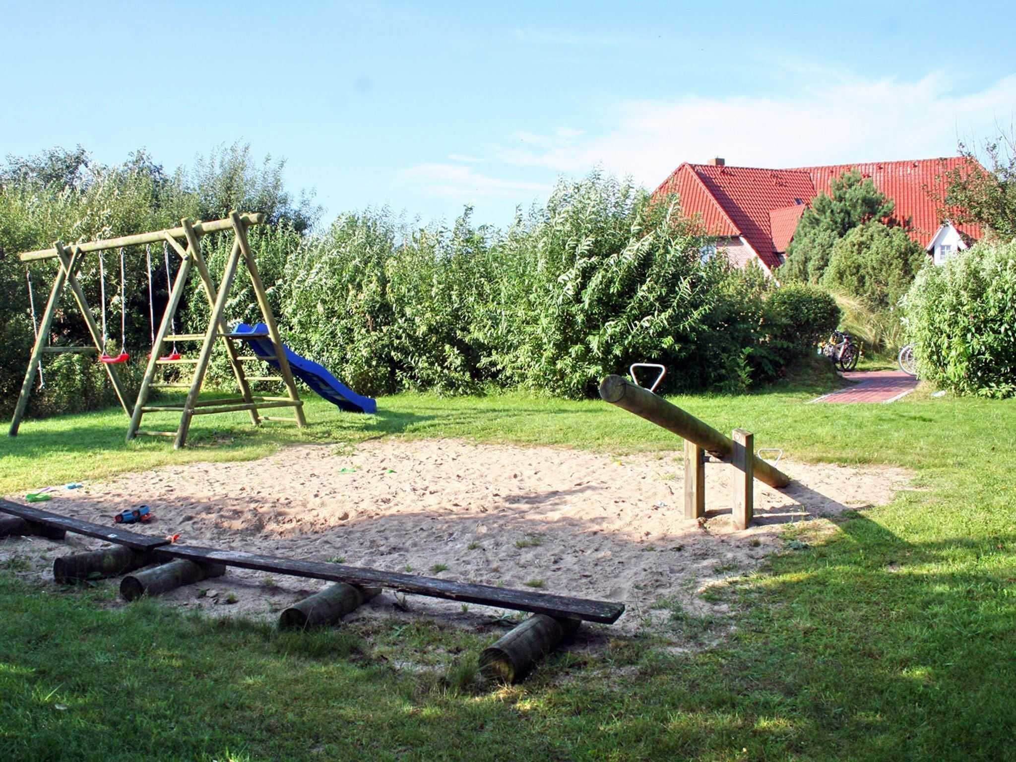 A playground with a swing set and a slide, surrounded by sand and grass.