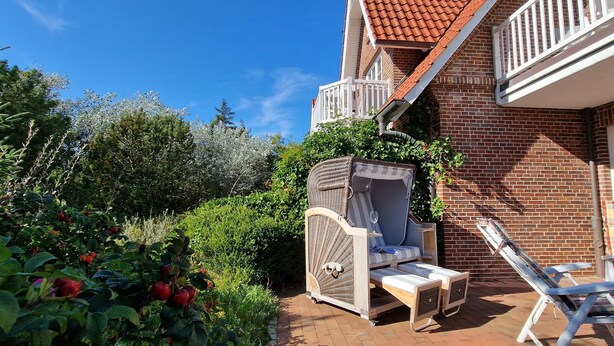 A patio with a wicker chair, a small table, and a glass of wine. - AH1a (room category) - Ahndole Hollken (Sankt Peter-Ording)