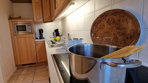 A kitchen with wooden cabinets, a microwave, a coffee maker, a sink, and a pot of spaghetti. - AH1a (room category) - Ahndole Hollken (Sankt Peter-Ording)