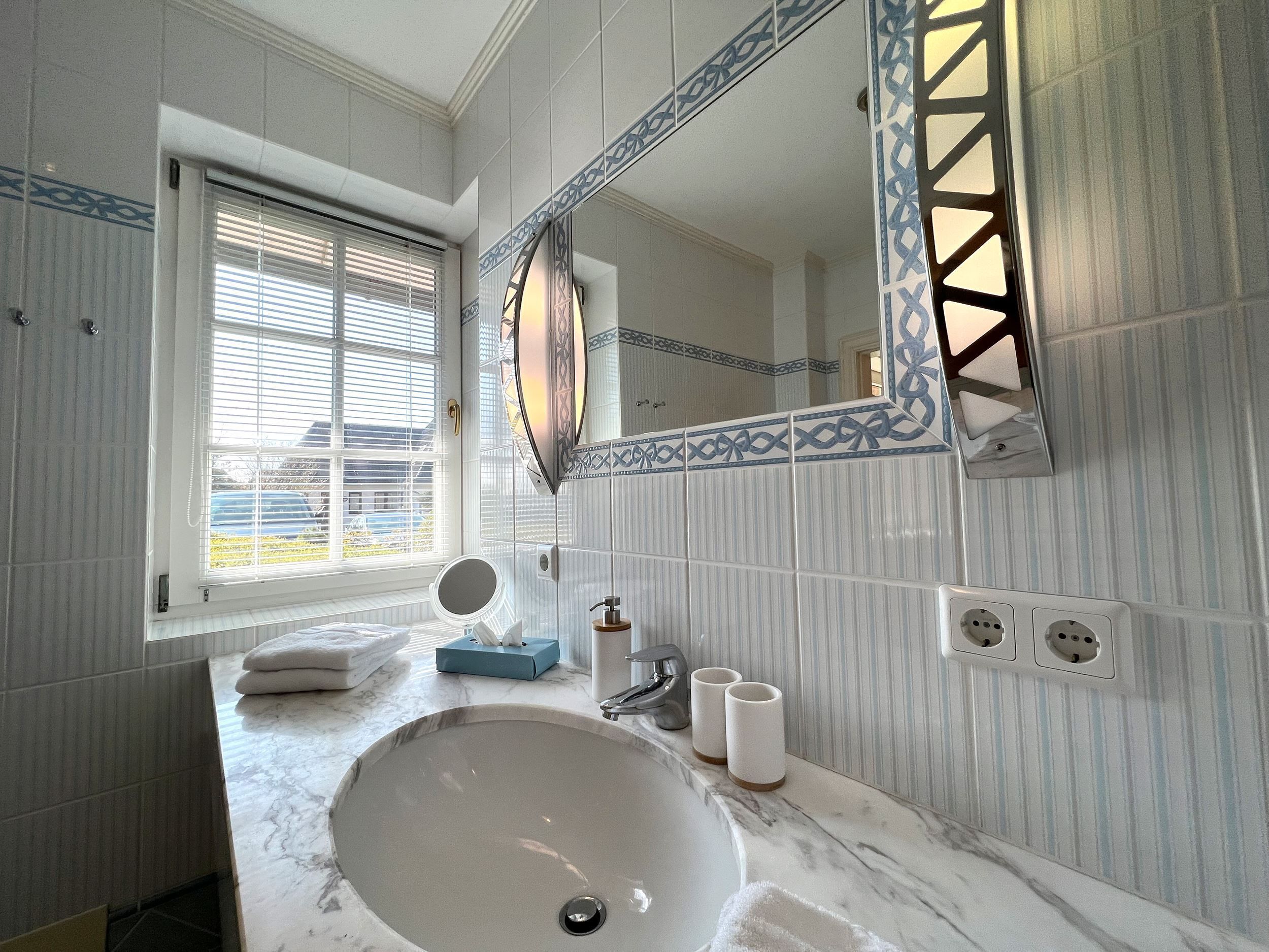 A bathroom with a large sink, a mirror, a window with blinds, and a towel rack.