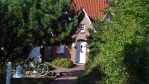 A traditional brick house with a red-tiled roof, a white door, and a bicycle parked in front. - AH1a (room category) - Ahndole Hollken (Sankt Peter-Ording)