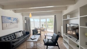 A living room with a sofa, coffee table, and chairs, a TV, and a painting on the wall. - Luna19 (Room category) - Luna II (Sankt Peter-Ording)