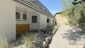 A building with a white exterior, a wooden bench outside, and a pathway leading to a door marked with the number 19. - Luna19 (Room category) - Luna II (Sankt Peter-Ording)
