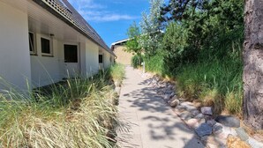A narrow pathway leading to a white building with multiple windows and a door marked '19'. - Luna19 (Room category) - Luna II (Sankt Peter-Ording)