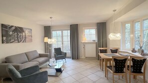 A modern living room with a sofa, a chair, a dining table with chairs, a lamp, and a painting on the wall.