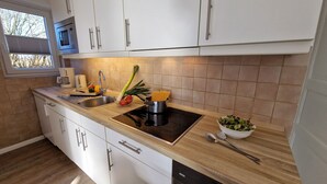 A modern kitchen with white cabinets, a stainless steel sink, and a black induction cooktop. - Luna31 (Room category) - Luna IV (Sankt Peter-Ording)