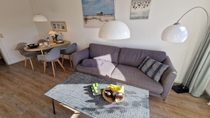 Ett modernt vardagsrum med en grå soffa, ett matbord med stolar och ett soffbord med frukt och ett glas vatten.