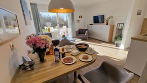 A modern dining area with a wooden table set for breakfast, including plates of food, cups, and a vase of flowers. - Luna31 (Room category) - Luna IV (Sankt Peter-Ording)