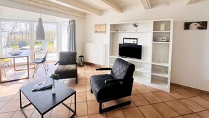 Un salon moderne doté d’un téléviseur, de sièges et offrant une vue sur l’extérieur.