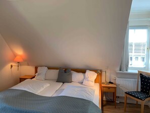 Ein Schlafzimmer mit einem Bett, zwei Nachttischen, einem Sessel, einem Fenster und einer Lampe.