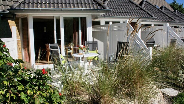 A house with a covered patio, a dining table, and chairs. - Luna18 (Room category) - Luna II (Sankt Peter-Ording)