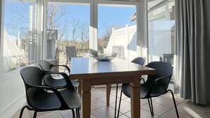 A dining area with a table and chairs, large windows, and a view of the outside. - Luna18 (Room category) - Luna II (Sankt Peter-Ording)