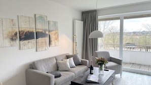 Una sala de estar moderna con un sofá gris, una mesa de centro con un jarrón de flores y un ventanal con vistas a una zona residencial.