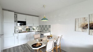 Una cocina moderna con armarios blancos, un microondas y una zona de comedor con una mesa para dos.