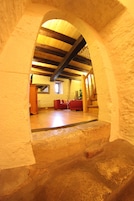 An arched stone corridor leading to a room with wooden beams, a red sofa, and a wooden cabinet.