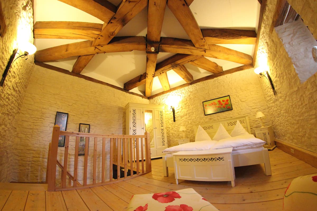 A bedroom with a wooden ceiling, a bed with white bedding, a nightstand, and a wall-mounted lamp.
