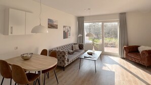 Un soggiorno moderno con divano, tavolo da pranzo e sedie. Si nota un'ampia finestra con tende, una lampada a soffitto e un'opera d'arte appesa al muro.