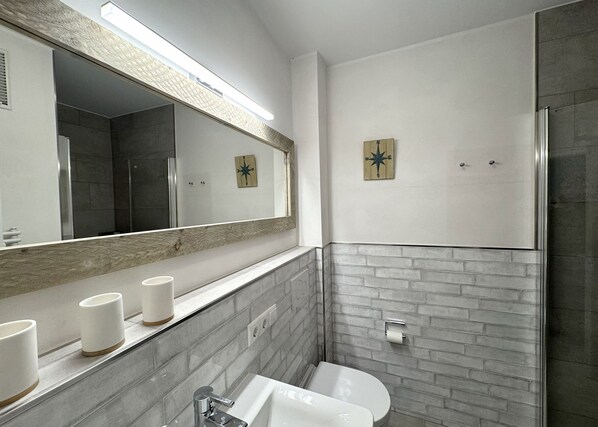 A modern bathroom with a large mirror, a sink, a toilet, and a shower area.
