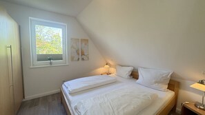 Ein Schlafzimmer mit einem Bett, einem Fenster, einem Nachttisch und einer Wandlampe.