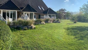 Una casa con tetto in tegole scure, un portico coperto con sedie e un prato curato.