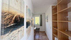 Un corridoio con opere d'arte alle pareti, una finestra con tende e una scaffalatura in legno.