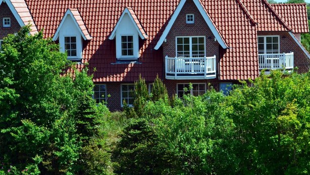 A large, multi-story house with a red-tiled roof, multiple windows, and balconies.