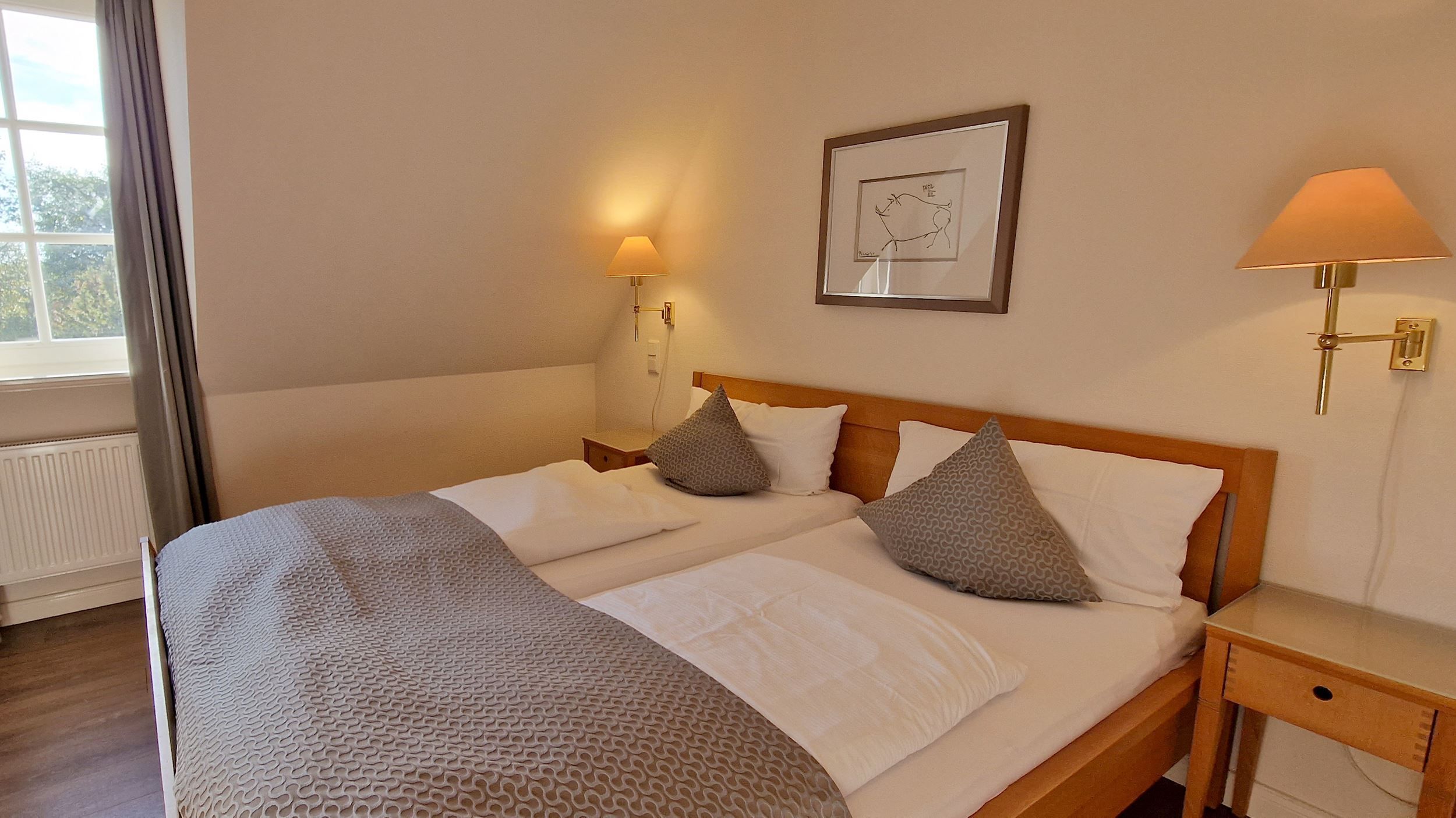 Een tweepersoonsbed met houten hoofdbord, twee nachtkastjes, een wandlamp en een ingelijst beeld aan de muur.
