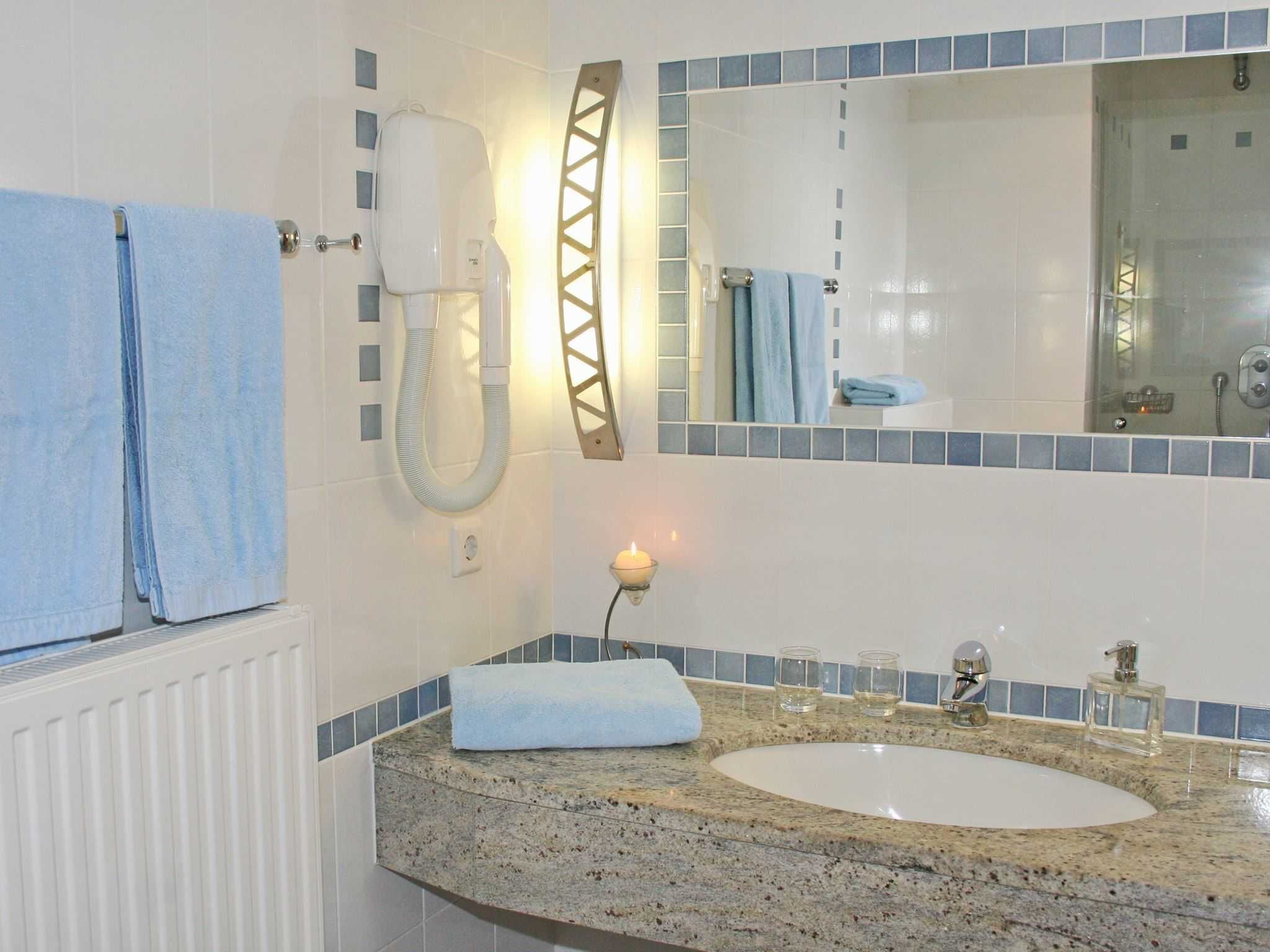 A bathroom with a white sink, a mirror, a towel rack, a hairdryer, and a small candle on the countertop.
