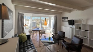 A modern living room with a leather sofa, a glass coffee table, and a dining area with a table and chairs. - Luna16 (Room category) - Luna II (Sankt Peter-Ording)
